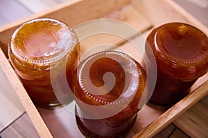 Top view of homemade apricot jam with pits and canned peach slices in glass jars upside down on wooden crate. Copy space