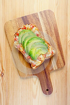 Top view of homemade grilled cheese toast topped with tomato and sliced avocado on wooden Breadboard