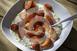 Top view. Homemade oatmeal porridge bowl with sliced strawberries on table in morning sunlight