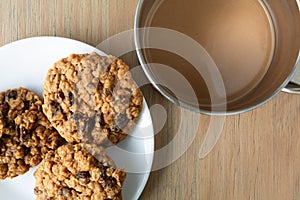 Top view of homemade oatmeal raisin cookies on a white plate and coffee atop a table illuminated with natural light