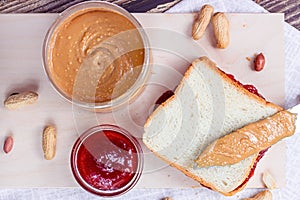 Top view of homemade sandwich for breakfast with fresh crunchy peanut butter and strawberry jelly on light background.