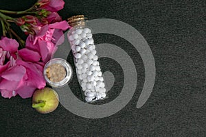 Top view of homeopathic pills bottles with wild fruit and pink flower on dark background. Natural Homeopathy Concept photo