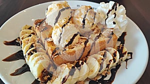 Top view of Honey toast topped vanilla ice cream and chocolate sauce served with banana slices and whipped cream on the white