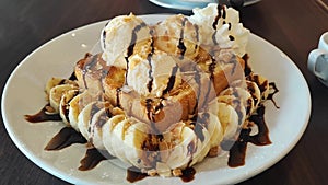 Top view of Honey toast topped vanilla ice cream and chocolate sauce served with banana slices and whipped cream on the white