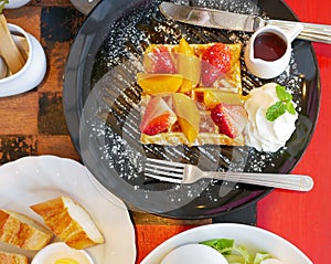 Top view of honey waffle with strawberry and peach and icing sprinkle in black plate on red table background