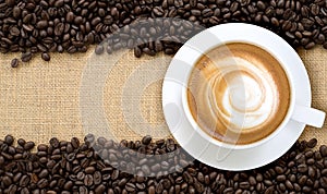 Top view of hot cappuccino with coffee beans on burlap background