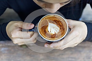 Top view of hot cappuccino coffee in the cafe, Heart shaped cream cappuccino coffee in blue cup. Hands women holding hot