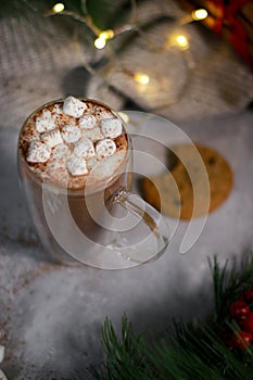 top view of hot chocolate in a glass mug with mini marshmallows on grey table, blurred xmas background