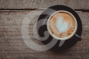Top view, Hot coffee, heart shape with milk latte on top of black ceramic cup on wooden table in coffee shop in vintage tone, copy