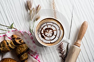 Top view hot coffee white cup beautifully decorated milk bubbles,bakery placed on white wood table,With sunshine in morning,