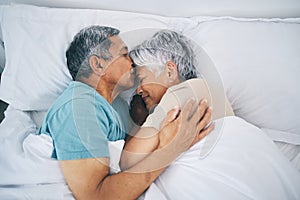 Top view, hug and senior couple in bed, love and sleeping with retirement, wake up or happiness with a kiss. Romance