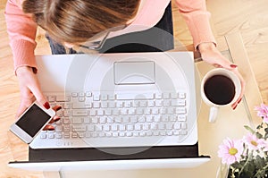 Top view of human hands, laptop keyboard, coffee, smartphone, on a wooden table