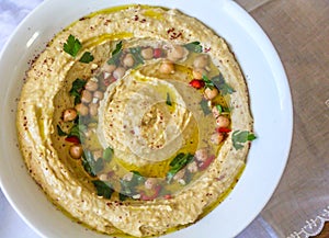 Top view of Humus plate garnished with fresh parsley leaves, red peppers bites, chickpeas, olive oil and sumac