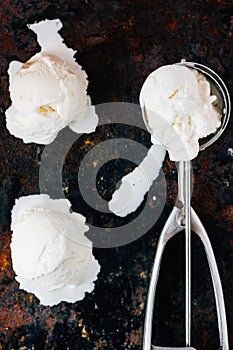 Top view of ice cream scooper with balls of ice cream on black rustic background.