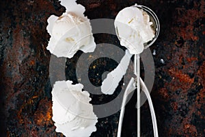 Top view of ice cream scooper with balls of ice cream on black rustic background.