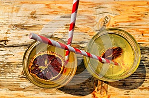 Top view of iced lemonades with dried orange slices and straws on a wooden table