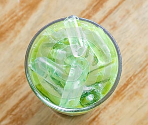 Top view of iced matcha latte or condensed milk-added green tea in transparent glass on blurred brown wood background