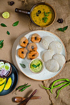 Top view of Idli, Wada, Sambar and Chutney. Traditional South Indian food, surrounded with lemon, raw mango and green chillies.