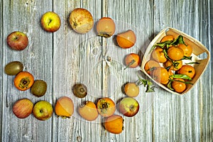 Top view image of apples, kiwis, ripe persimmons, pomegranates and basket wooden table