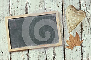 Top view image of autumn leaves and fabric heart next to chalkboard over wooden textured background. copy space