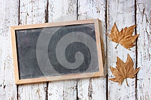 Top view image of autumn leaves next to chalkboard over wooden textured background. copy space