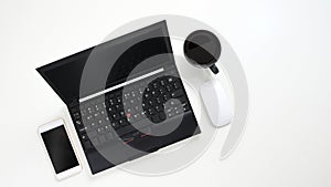 Top view image of Black computer laptop putting on white table with coffee cup, cropped white smartphone and wireless mouse.