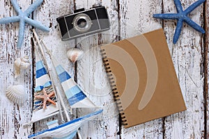 Top view image of blank notebook, wooden sailboat, starfish, shells and camera. travel and adventure concept