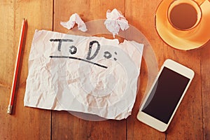 Top view image of blank paper with the text to do in hand write, next to cellphone and coffee cup over wooden table