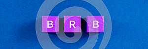 Top view image of BRB spelled on violet wooden dices. Over blue background