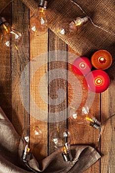 Top view image with bulblight garland, glowing candles and sackcloth bag on raw rustic background.