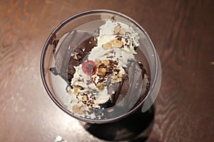 Top view image of Chocolate ice cream in a bowl with whipped cream.Hand holding a red cherry and put it on the top of chocolate