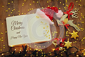 Top view image of christmas festive decorations next to open notebook on old wooden background.