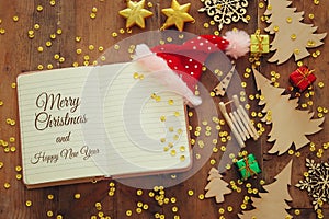 Top view image of christmas festive decorations next to open notebook on old wooden background.