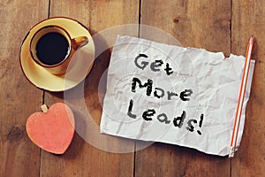 Top view image of coffee cup, heart shape and paper with the phrase get more leads over wooden background