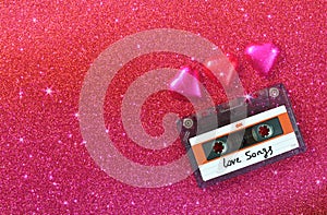 Top view image of colorful heart shape chocolates and audio cassette on red glitter background