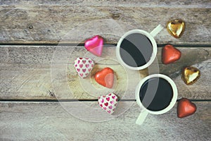 Top view image of colorful heart shape chocolates, fabric heart and couple mugs of coffee on wooden table