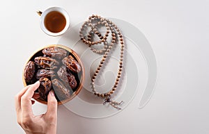 Top view image of decoration Ramadan Kareem background,  hands picking up dates fruit, tea and rosary beads. Flat lay background