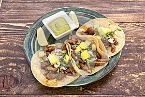 Top view image of delicious Mexican al pastor tacos with lime wedges, corn tortillas and some guacamole on a beautiful green plate