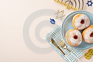 Top-view image featuring customary Jewish delicacies sufganiyot, napkin, cutlery, Star of David, menorah, gelt on beige surface