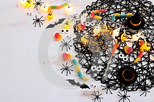 top view image of Halloween holoday. witcher broom, treats, spiders and bats over white wooden table