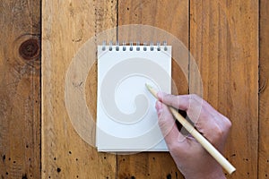 Top view image of a hand holding a pen and going to write on a blank white notebook