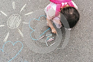 Top view image of happy little girl wears pink dress and backpack drawing with colorful chalks on the sidewalk. Cute child