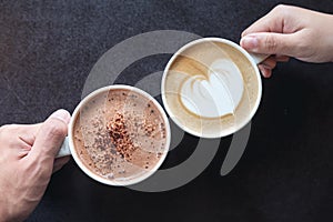 Man and woman`s hands holding coffee and hot chocolate cups with wooden table background