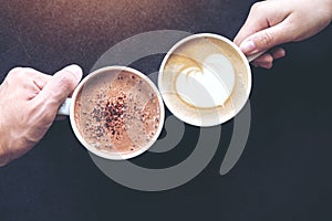 Man and woman`s hands holding coffee and hot chocolate cups with wooden table background