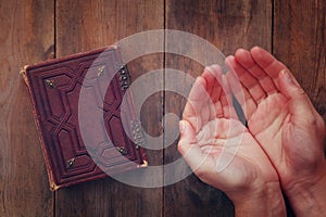 Top view image of mans hands folded in prayer next to prayer book. concept for religion, spirituality and faith