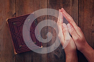 Top view image of mans hands folded in prayer next to prayer book. concept for religion, spirituality and faith