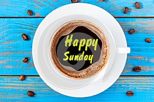 Top view image of morning coffee cup with phrase: happy sunday on blue wooden background. Weekend breakfast concept