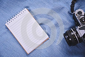 top view image of open notebook with blank pages and camera on blue blackground.