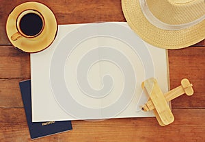 Top view image of open notebook with blank pages, cup of coffee wicker hat and wooden aeroplane over wooden table. ready for