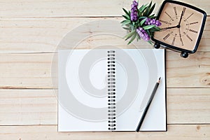 Top view image of open notebook with blank pages and retro alarm clock on wooden background, ready for adding or mock up